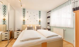 A bright bedroom with a large bed and modern furniture.  
On the wall are decorative butterflies and there is plenty of daylight through the window.