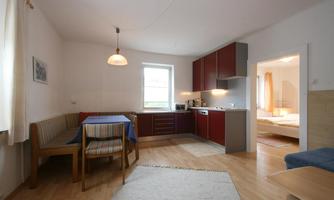 A cozy kitchen with a dining area and modern appliances. The room has warm lighting and access to an adjacent bedroom.
