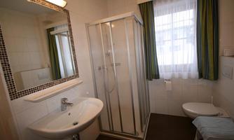 A modern bathroom with a shower, a sink, and a white toilet seat. Bright walls and a window provide natural lighting.