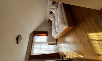 A cozy bedroom with a double bed and hardwood floor. Bright windows let in plenty of light.