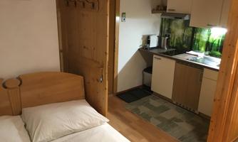 A cozy room with a double bed and a small kitchenette. The decor is wood and bright, with green accents in the kitchen.