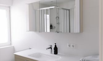 A modern bathroom with a bright wood vanity and a large mirror. Towels are neatly stacked and a window provides plenty of natural light.