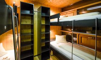A cozy sleeping area with bunk beds and wooden interior. Two shelves are placed in the middle of the room, providing additional storage space.