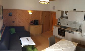A cozy kitchen with a dining area and a living room. The walls are made of wood, and the decor is modern and inviting.