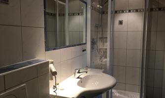A modern bathroom with a shower, a sink, and a mirror. The walls are brightly tiled and the lighting is pleasant.