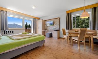 A modern room with a double bed and table. The room has large windows with a view of the mountains and is bright and cheerfully furnished.