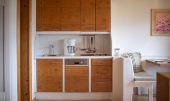 A modern kitchen with wooden fronts and white design. It is well-equipped and offers a cozy dining area.