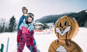 A cheerful skiing scene in the snow with two children. In the foreground stands a funny snow figure.