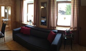 A cozy living room with a black sofa and red cushions. Large windows let in plenty of light and provide a view outside.