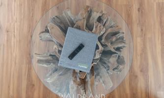A gray notebook is lying on a round glass table, surrounded by a wooden structure. The table is on a wooden floor and conveys a modern atmosphere.