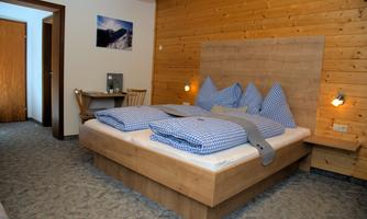 A cozy bedroom with a wooden bed and checked bedding. The walls are made of wood, and there is a small workspace nearby.