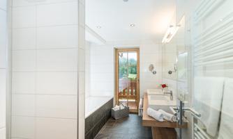 A modern bathroom with bright tiles and a large window. There is a bathtub, two sinks, and fresh towels.