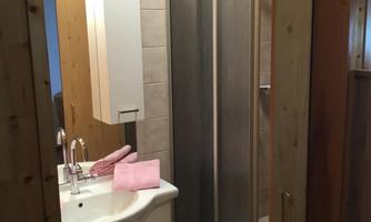 A modern bathroom with a sink and a shower enclosure. The walls are tiled in light colors and there are wooden details.