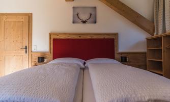 A cozy bedroom with two single beds and wooden details. On the wall hangs a picture featuring a stag motif.