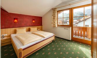 A cozy bedroom with two single beds and a colorful carpet. Large windows provide a view outside and ample daylight.
