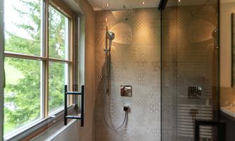 A modern shower with a glass cabin and elegant design. Through the window, there is a view of a green tree.