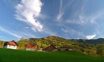 A picturesque village in the countryside, surrounded by green meadows and mountains. The sky is clear with gentle clouds.