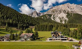A picturesque landscape with green meadows and tall mountains in the background. Nearby are several charming buildings.