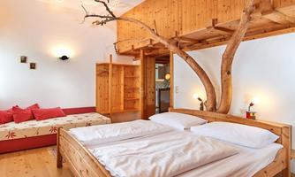 A cozy room with wooden interiors and a large double bed. A tree trunk is creatively integrated into the room, adding a natural atmosphere.