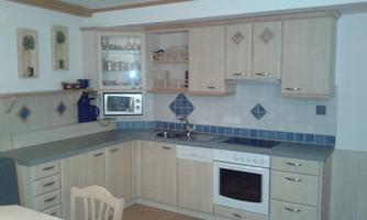 A modern kitchen with wooden cabinets and blue tiles. The equipment includes an oven, a microwave, and a sink.