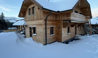 A wooden house in the snow, surrounded by mountains. The landscape depicts a serene winter idyll.