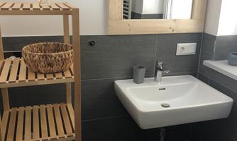 A modern bathroom with a sink, a wooden shelf, and a mirror. The walls are in dark gray, and there are towels on the shelf.