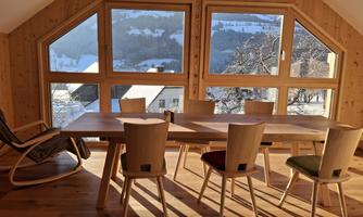A bright dining area with a large table and modern chairs. Large windows provide a beautiful view of the snow-covered landscape.