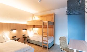 A modern room with a bunk bed and a single bed. The room has a minimalist style with wooden details and a desk.