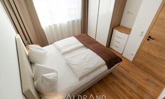 A cozy bedroom with a double bed and large windows. The room has a modern style and light wood flooring.
