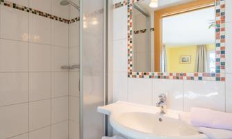A modern bathroom with a glass door shower and a white sink. The walls are decorated with light tiles and a colorful border.