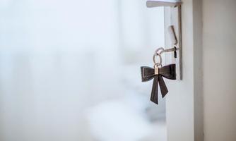A key with a looped keychain hangs on a door. In the background, a blurred room is visible.
