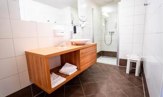 A modern bathroom with a wooden shelf and a shower. The walls are brightly tiled, and fresh towels are laid out.