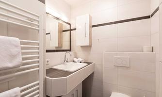A modern bathroom with bright tiles and a sleek sink. Towels hang neatly on a towel heater.