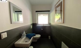 A modern bathroom with a sink, a toilet, and a window. The walls are in neutral colors and there are decorative elements like mirrors and artworks.