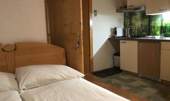 A cozy room with a double bed and a kitchenette. The furnishings are made of wood and create a warm atmosphere.