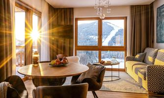 A cozy living room with a table full of fresh fruits and a view of the snow-covered mountains. The warm light of the evening sun shines through the large windows.