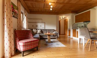 A cozy living space with a red checkered chair, a wooden table, and a gray sofa. The wooden beam ceiling and the warm wooden floor give the room an inviting atmosphere.