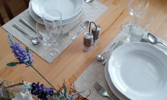 A set table with two white plates, glasses, and cutlery. A decorative flower arrangement is in the center.