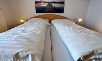 A cozy bedroom with two beds and soft blankets. On the wall hangs a picture of a pier by the water.