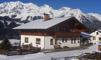 A charming Alpine-style house is situated in a snow-covered landscape. Majestic mountains can be seen in the background.