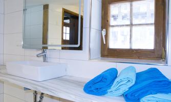 A modern bathroom with a sleek sink and a large mirror. Several turquoise towels are laid out on the shelf.