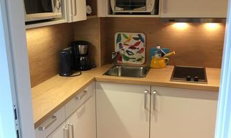 A modern kitchen with white cabinets and wood surfaces. There is a sink, microwave, and stove as well as some kitchen appliances.