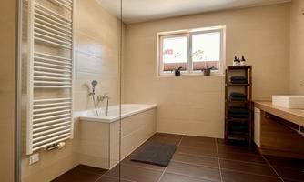 A modern bathroom with a bathtub and a shower. Large windows provide plenty of natural light and a pleasant atmosphere.
