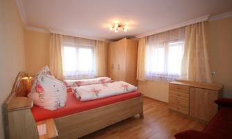 A cozy bedroom with a double bed and bright curtains. There is a wooden wardrobe and a dresser.