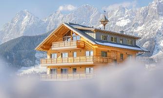 A cozy wooden house in a winter landscape. The mountains in the background are snow-covered and the sky is clear.