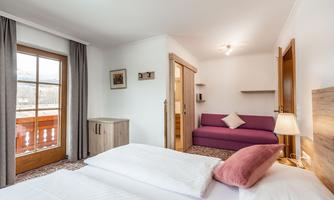 A bright room with two single beds and a cozy sofa. The window offers a view of the surroundings and lets in plenty of natural light.