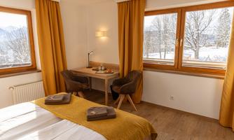 A bright bedroom with large windows and a view of the winter landscape. The warm curtains and modern furnishings create a cozy atmosphere.