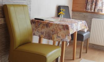A cozy dining area with a small table and two chairs. On the table, there is a vase with a flower.