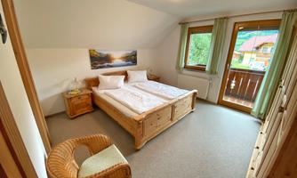 A cozy bedroom with a wooden double bed. Large windows and a picturesque view create a bright, inviting atmosphere.