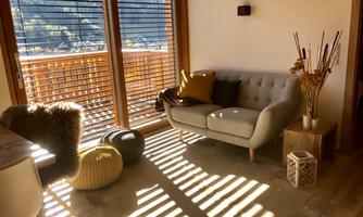 A cozy living room with a bright sofa and colorful poufs. Sun rays are coming through the windows, warming the room.